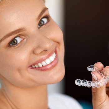 A girl smiles while holding her Invisalign in her hands